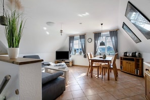 Un salon comprenant un canapé, un téléviseur, une table à manger, des chaises et une plante.