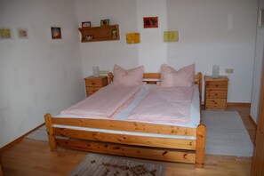 Ein Doppelbett mit Holzrahmen, zwei Nachttische, ein kleines Regal mit Bildern und ein weißer Teppich auf dem Boden.
