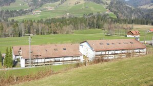 Ein ländliches Gebäude mit einem geneigten Dach, umgeben von grünen Feldern und Hügeln.