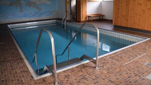 Ein Innenpool mit gefliesten Wänden, einer Holzbank und einem Wandbild von Delfinen.