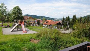 Ein Spielplatz mit Rutsche und Schaukeln, umgeben von Häusern und Grünflächen.