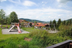 Ein Spielplatz mit Rutsche und Schaukeln, umgeben von Häusern und Grünflächen.