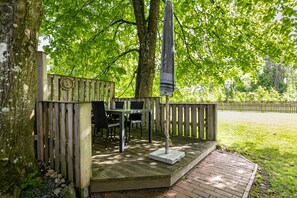 Une terrasse en bois, agrémentée d’une table et de chaises, entourée d’une clôture en bois, et située dans un cadre verdoyant luxuriant.