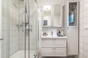 Une salle de bain dotée d’une douche à parois de verre, de meubles blancs et d’un miroir au-dessus du lavabo.