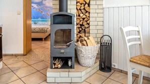 Ein Kaminofen mit Backsteingrundlage, ein Korbkorb mit Holz und ein weißer Stuhl.