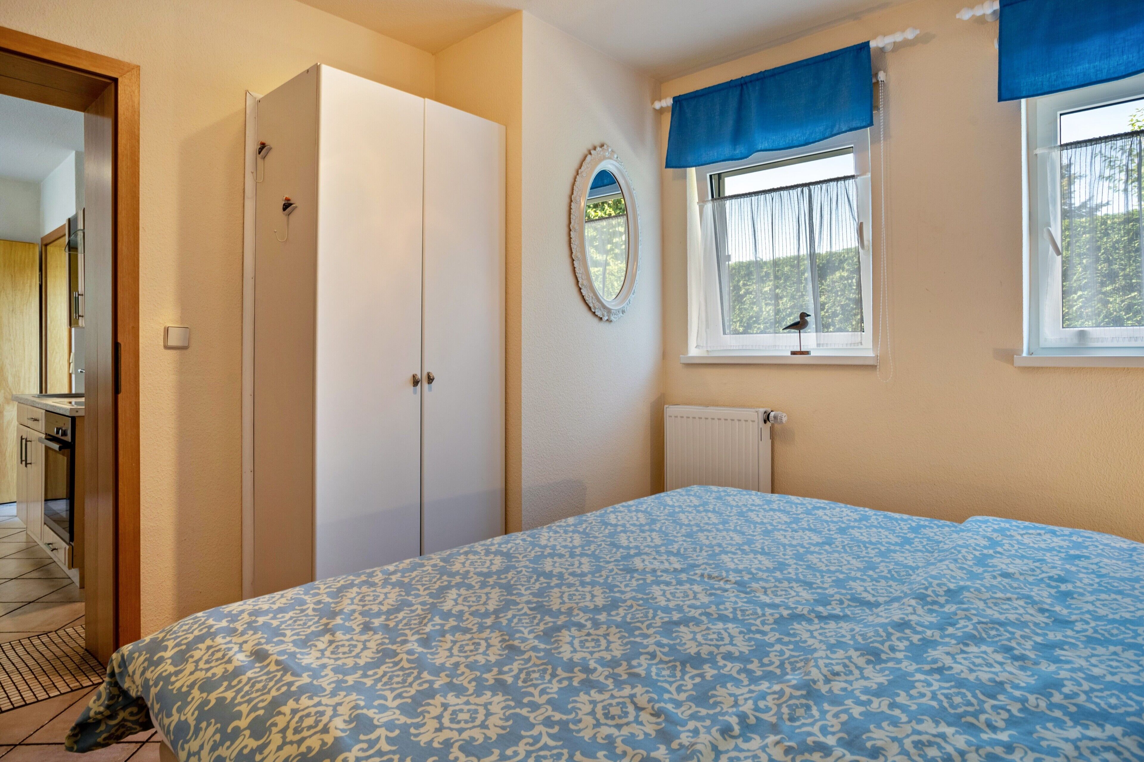 Een slaapkamer met een bed, een kledingkast, een raam met gordijnen en een radiator.