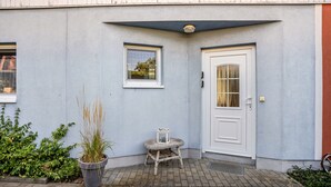 Eine Gebäudeecke mit einer weißen Tür, einem kleinen Fenster und einem Laternenschirm auf einem Hocker.