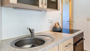 Eine Küche mit Spüle aus Edelstahl, Holzschränken, einem eingebauten Backofen und einem Schrank mit Glasfront über der Spüle.