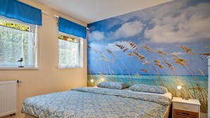 Ein Schlafzimmer mit einem Bett, zwei Fenstern, einem Wandbild und einem Nachttisch.