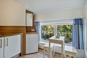 Una cocina compacta con ventana, una mesa pequeña y muebles blancos.