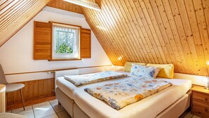 Ein Schlafzimmer mit schrägem Dach, einem Bett mit floralem Bettzeug, einem Fenster mit Aussicht und einem Holzboden.