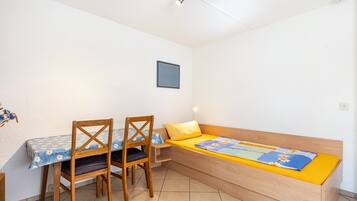 Une petite pièce avec un lit en bois, une table avec des chaises et un seul luminaire fixé au mur.