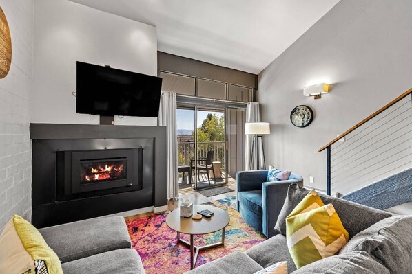 A modern living room with a fireplace, a flat-screen TV, a sofa, and a colorful rug.