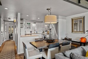 A modern kitchen with white cabinetry, a wooden dining table, and a large pendant light.