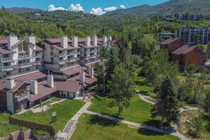 A multi-story hotel with balconies, surrounded by greenery and hilly terrain. - Walk to Mtn w/Hot Tub! Elevator-W/D-Epic Views! (Steamboat Springs)