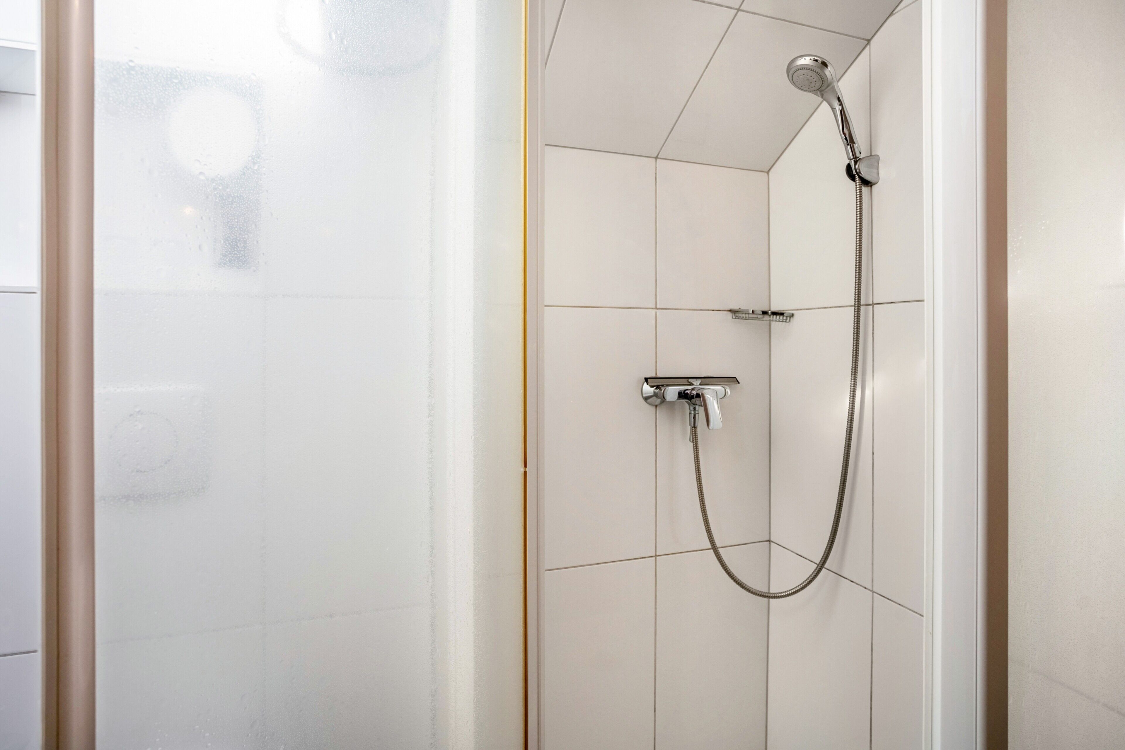 Une douche équipée d’un pommeau de douche à main et d’un pommeau de douche fixe fixé au mur, les deux étant reliés à des tuyaux.