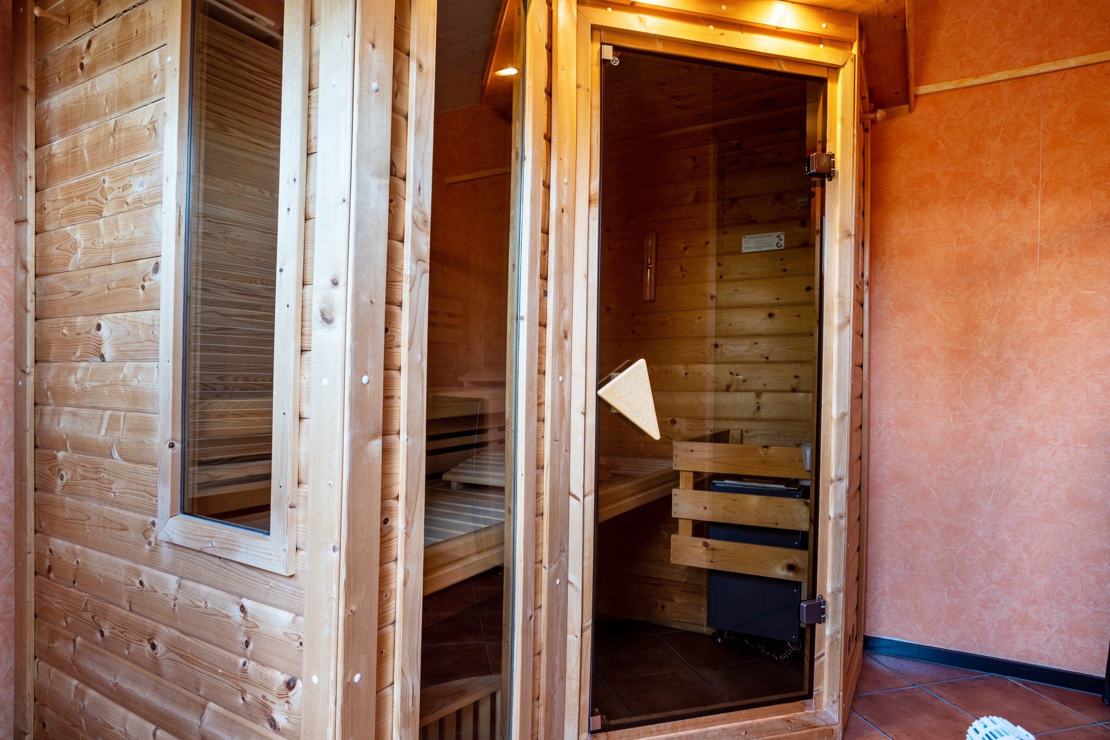 Una cabaña de madera con puerta de cristal, una ventana y un banco de madera en su interior.