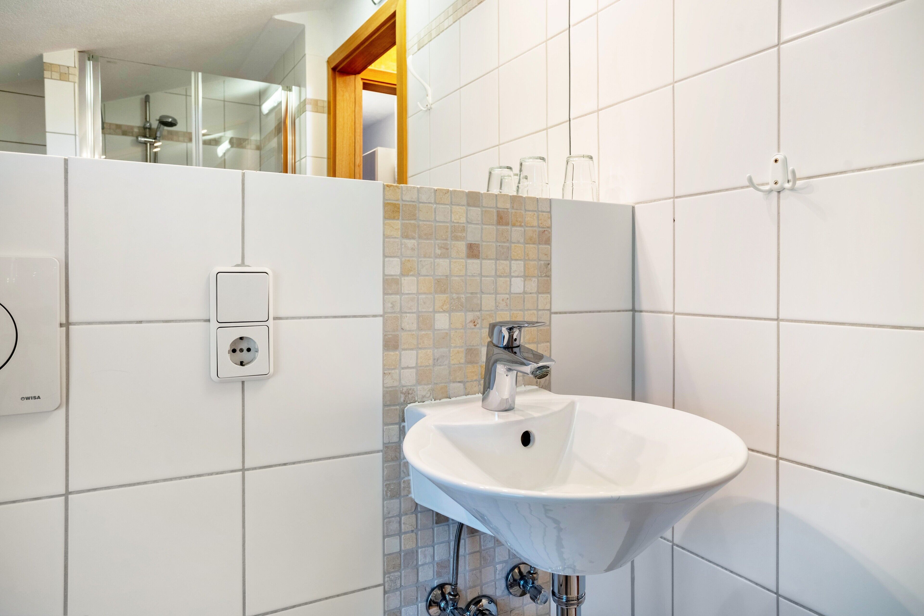 Ein Badezimmer mit einem weißen Waschbecken, einem Spiegel und einer gefliesten Wand.