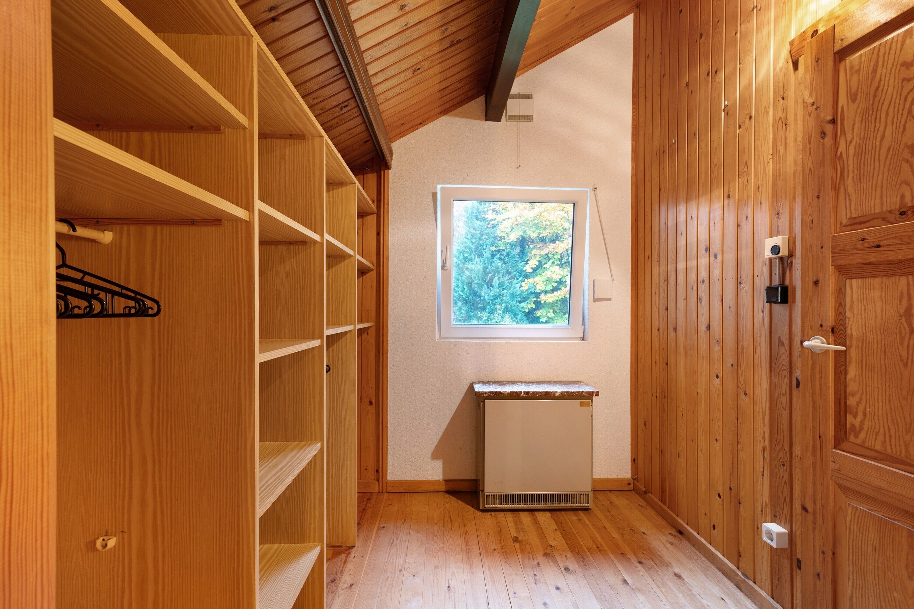 Un intérieur en bois avec un radiateur, une fenêtre donnant sur des arbres et une porte.