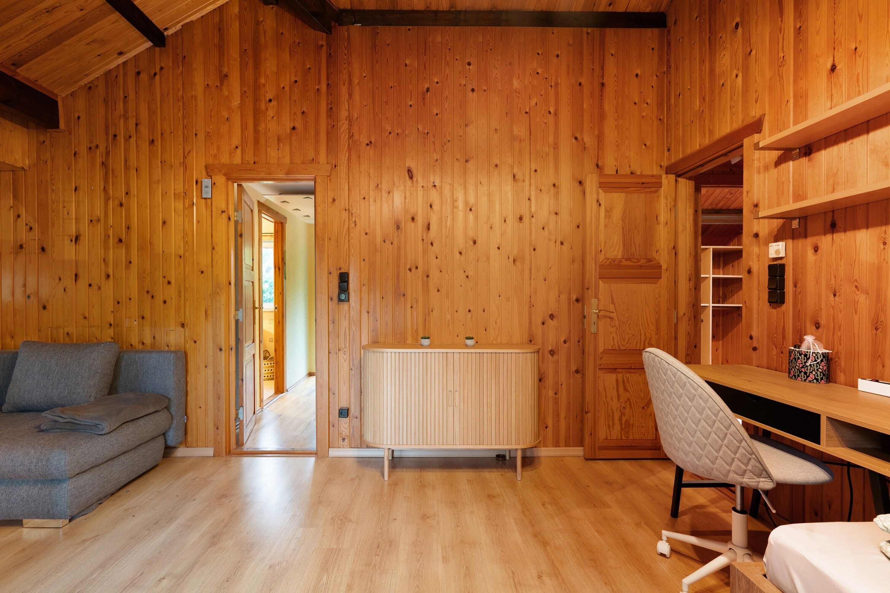 Una habitación con paredes de madera, un sofá, un escritorio con una silla y un radiador.