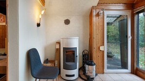 Una habitación con estufa de leña, una silla, un aspirador y un vidrio corredizo que da al exterior.