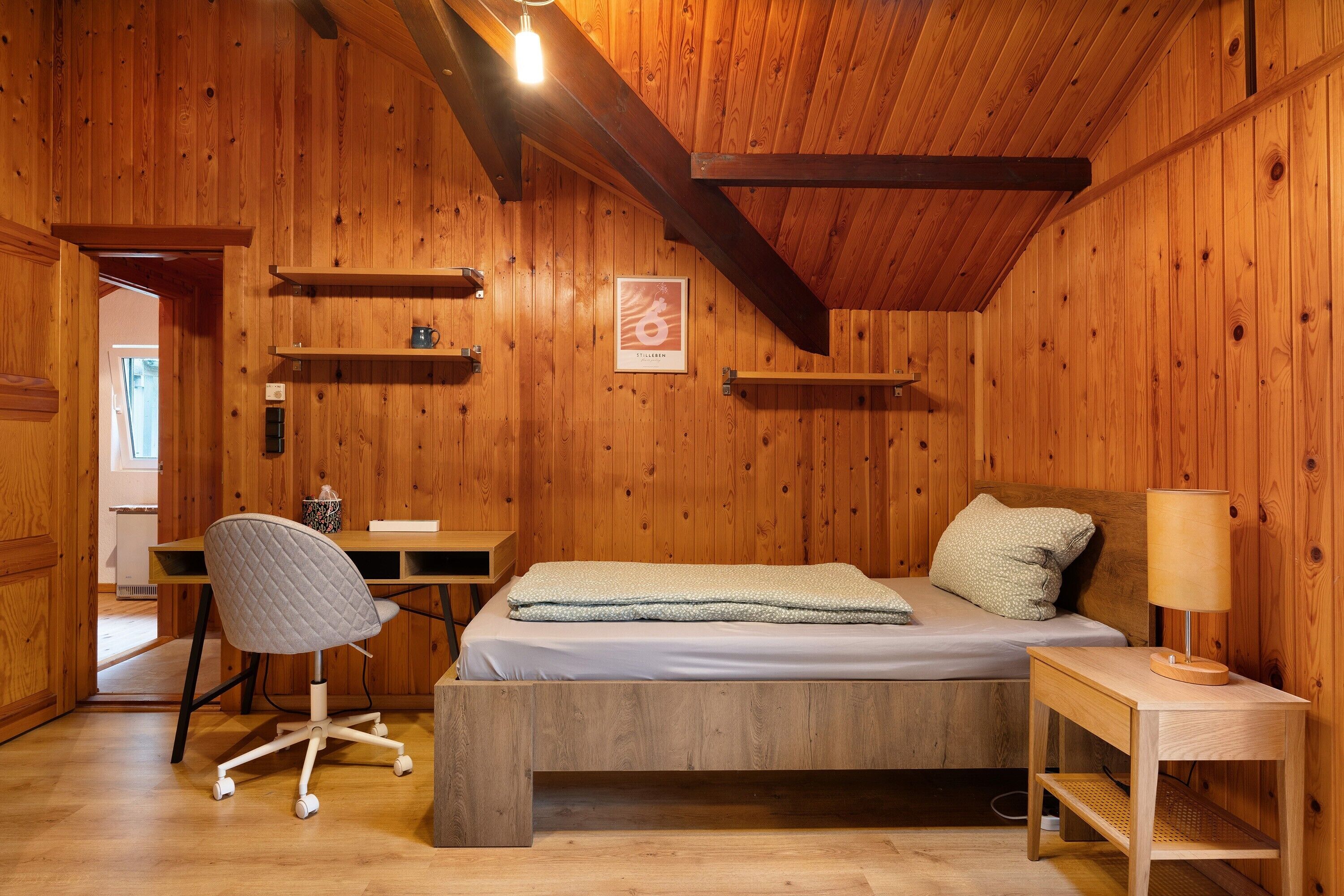 A wooden room with a bed, desk, chair, and shelves.