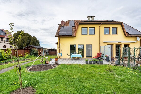 A yellow house with solar panels, a garden, and a patio with outdoor furniture. - Apartment 'Fewo Energiepunkt Am Planitzwald' with Private Terrace, Private Garden and Wi-Fi (Bennewitz)