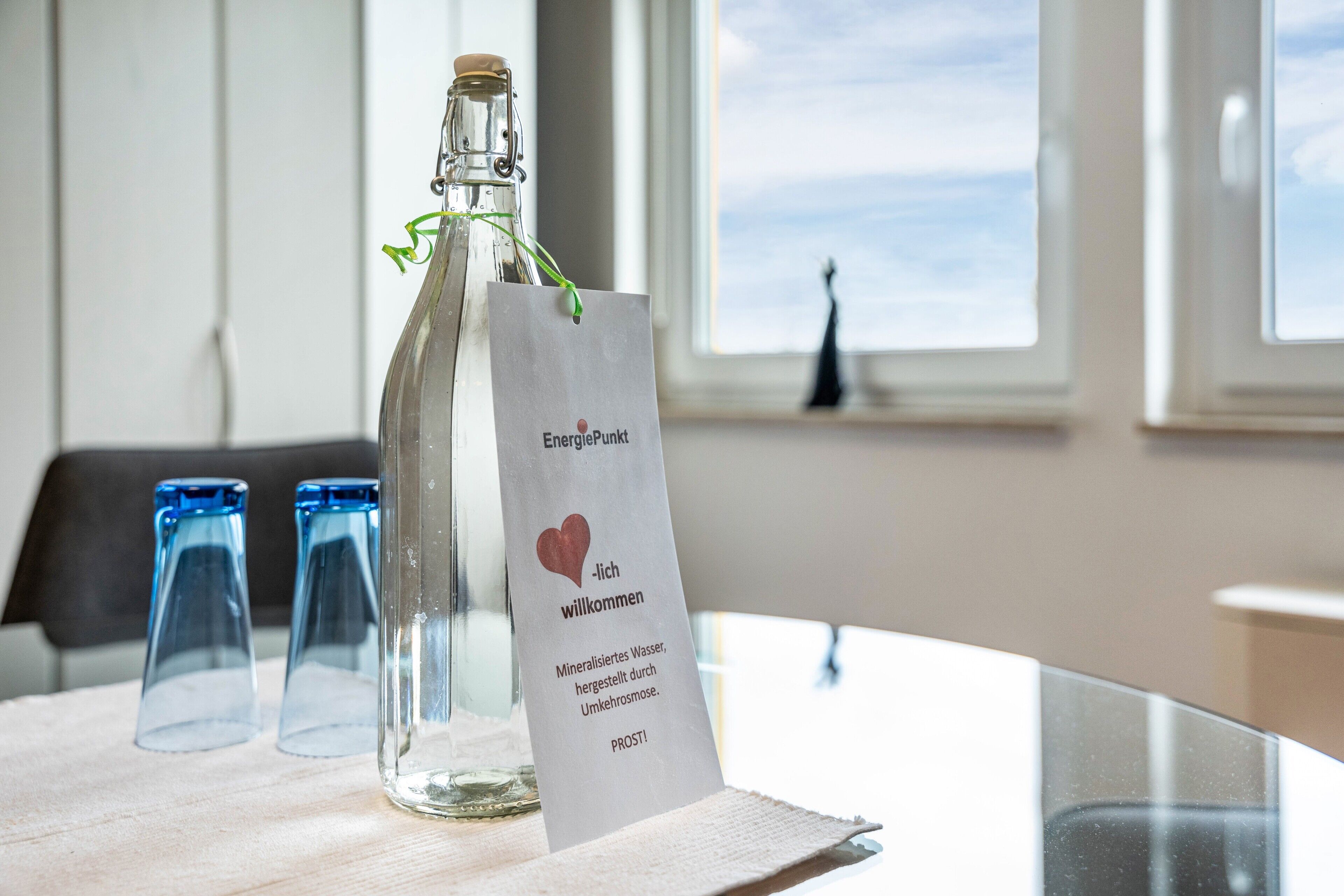 A bottle of water with a label, two empty glasses, and a window view.