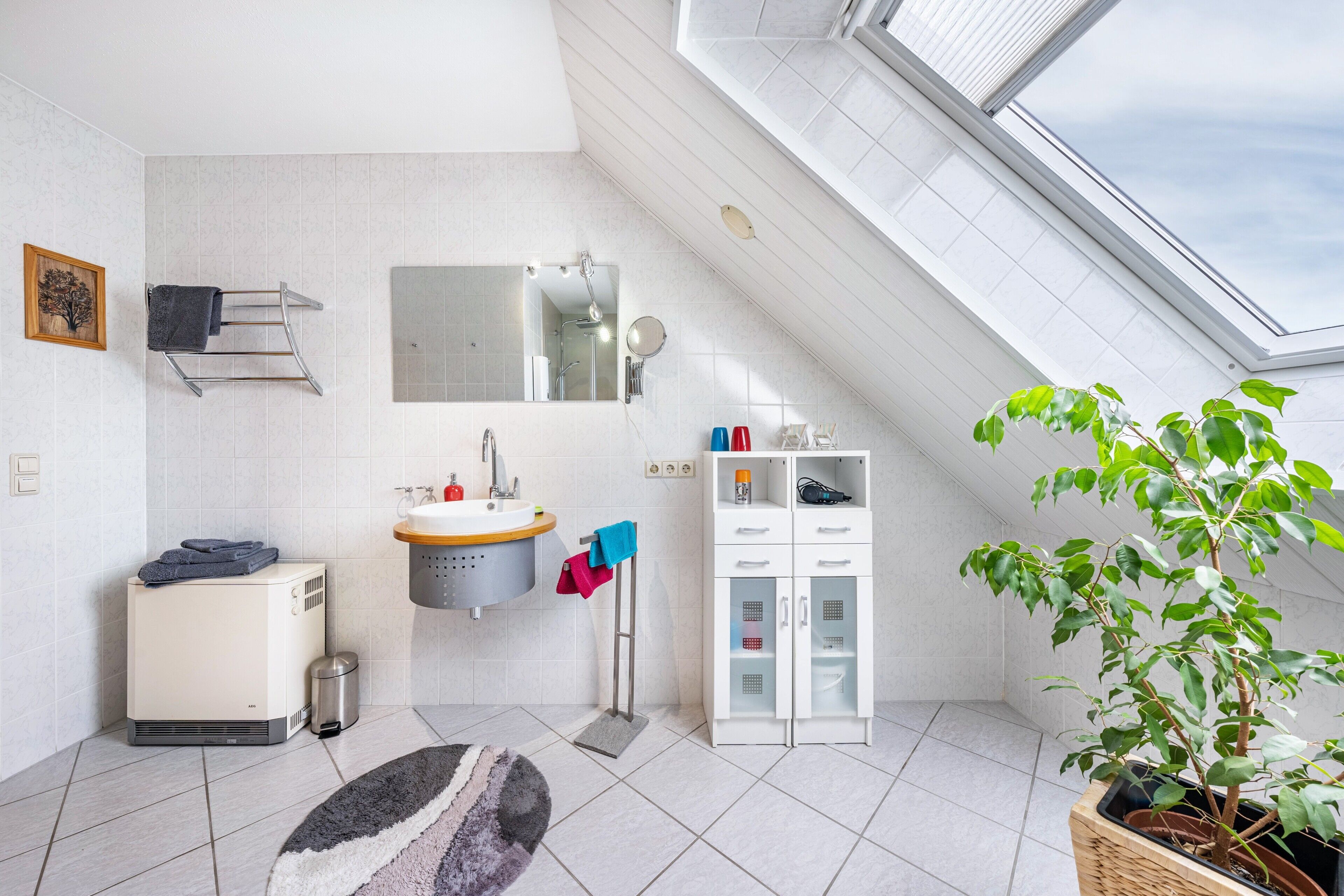 A modern bathroom with a skylight, a sink, a mirror, a towel rack, a cabinet, and a potted plant.