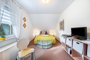 A bedroom with a bed, a TV, a chair, a glass table, and storage units. - Apartment 'Fewo Energiepunkt Am Planitzwald' with Private Terrace, Private Garden and Wi-Fi (Bennewitz)