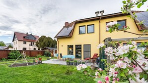 Una casa amarilla con jardín, un columpio y una mesa con sillas afuera.