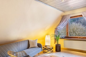 Une pièce chaleureuse avec un canapé, une plante en pot, une lampe et une vue par la fenêtre.