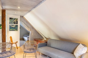Une pièce de style loft avec un canapé gris, des fauteuils en osier, une table en bois et un escalier.