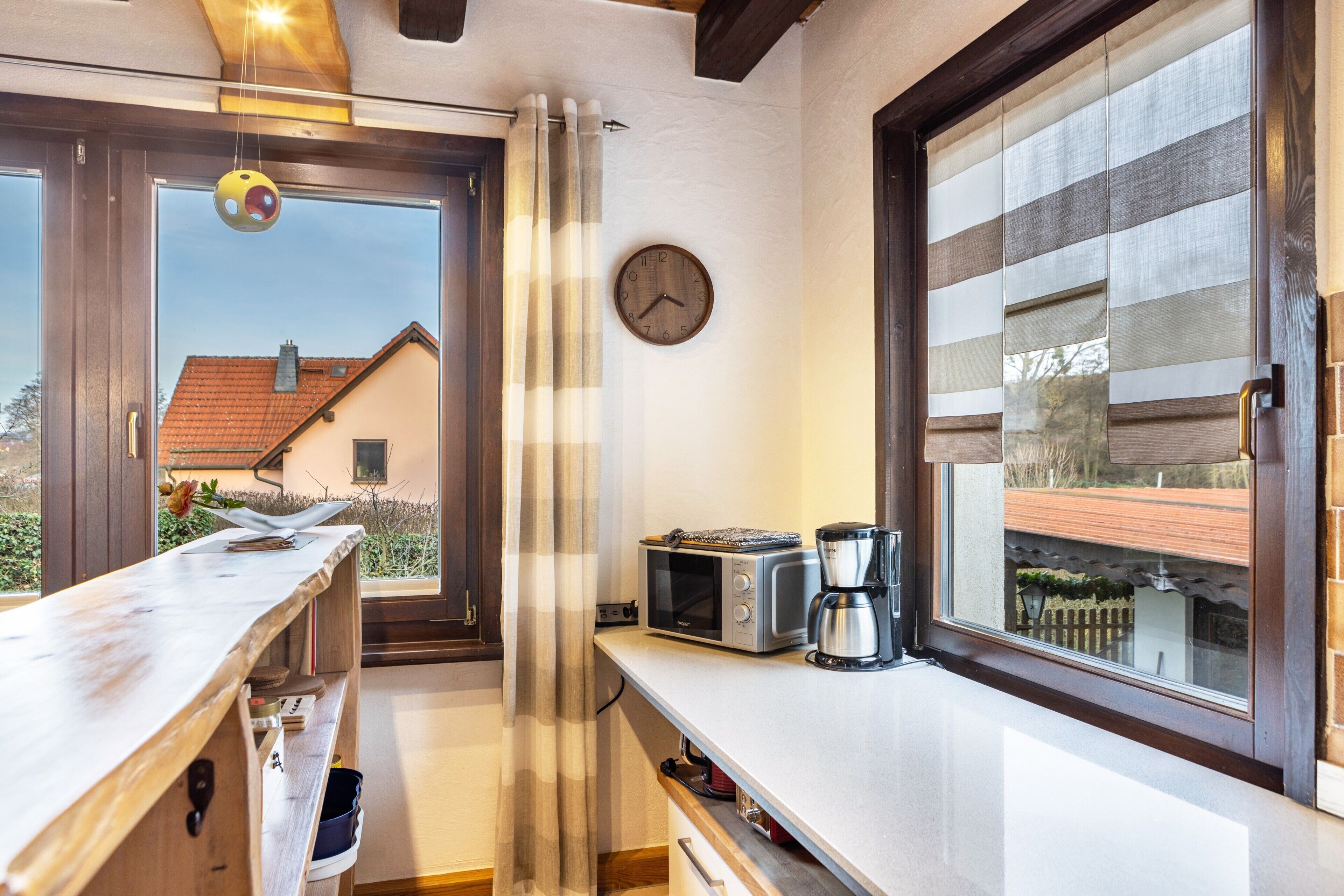 A kitchen with a window, a clock, a microwave, and a coffee maker.