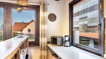 A kitchen with a window, a clock, a microwave, and a coffee maker.