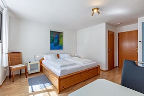 A bedroom with a wooden bed, a nightstand, a chair, a painting on the wall, and a door. - Room 'Zimmer 1' with Shared Terrace, Shared Garden and Wi-Fi (Schönau im Schwarzwald)