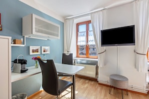Quarto com uma mesa de jantar, cadeiras, televisão e janela com cortinas.