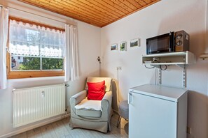 Une petite pièce avec une chaise, un radiateur blanc, un four à micro-ondes et une fenêtre avec des rideaux.