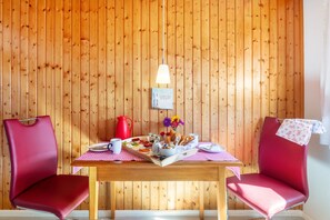 A wooden-paneled room with a table set for breakfast, two red chairs, a red kettle, and a hanging light fixture.