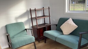 Una habitación con un sillón verde, un sofá a juego con un cojín, y una mesita de madera.