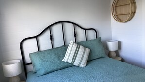 Una cama bien hecha con una colcha azul estampada y dos almohadas, con dos lámparas de noche de madera a cada lado.