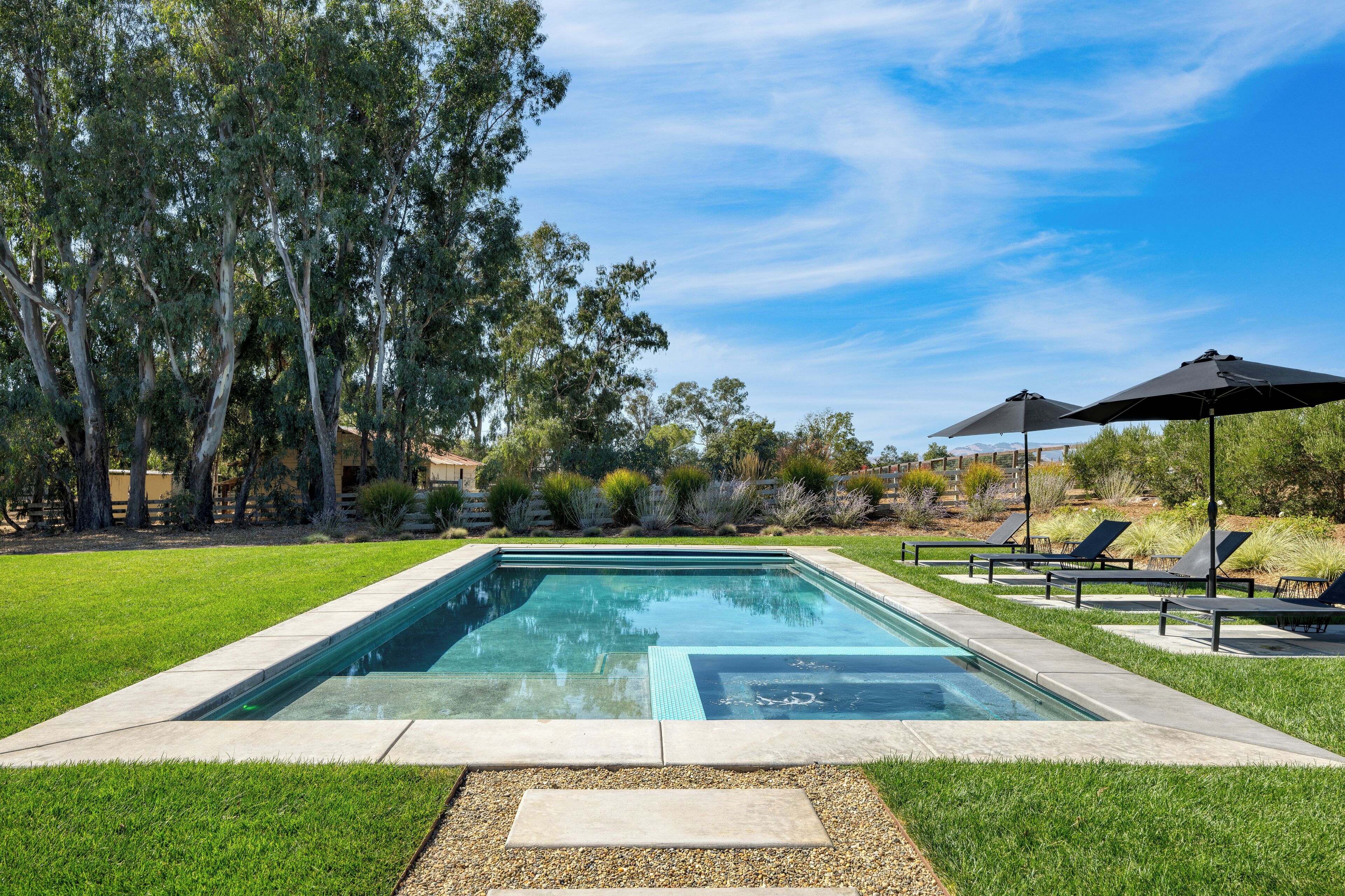 A rectangular swimming pool with a clear blue water surface, surrounded by a well-maintained lawn and trees.