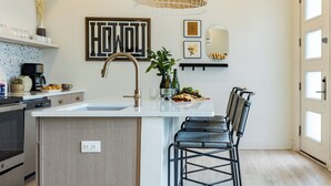 Una cocina moderna con una isla central, taburetes negros tipo bar, una lámpara colgante y un letrero en la pared con la palabra 'HOWL'.