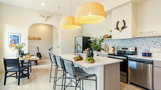 Una cocina moderna con una isla central, taburetes de bar y elegantes lámparas colgantes de mimbre.