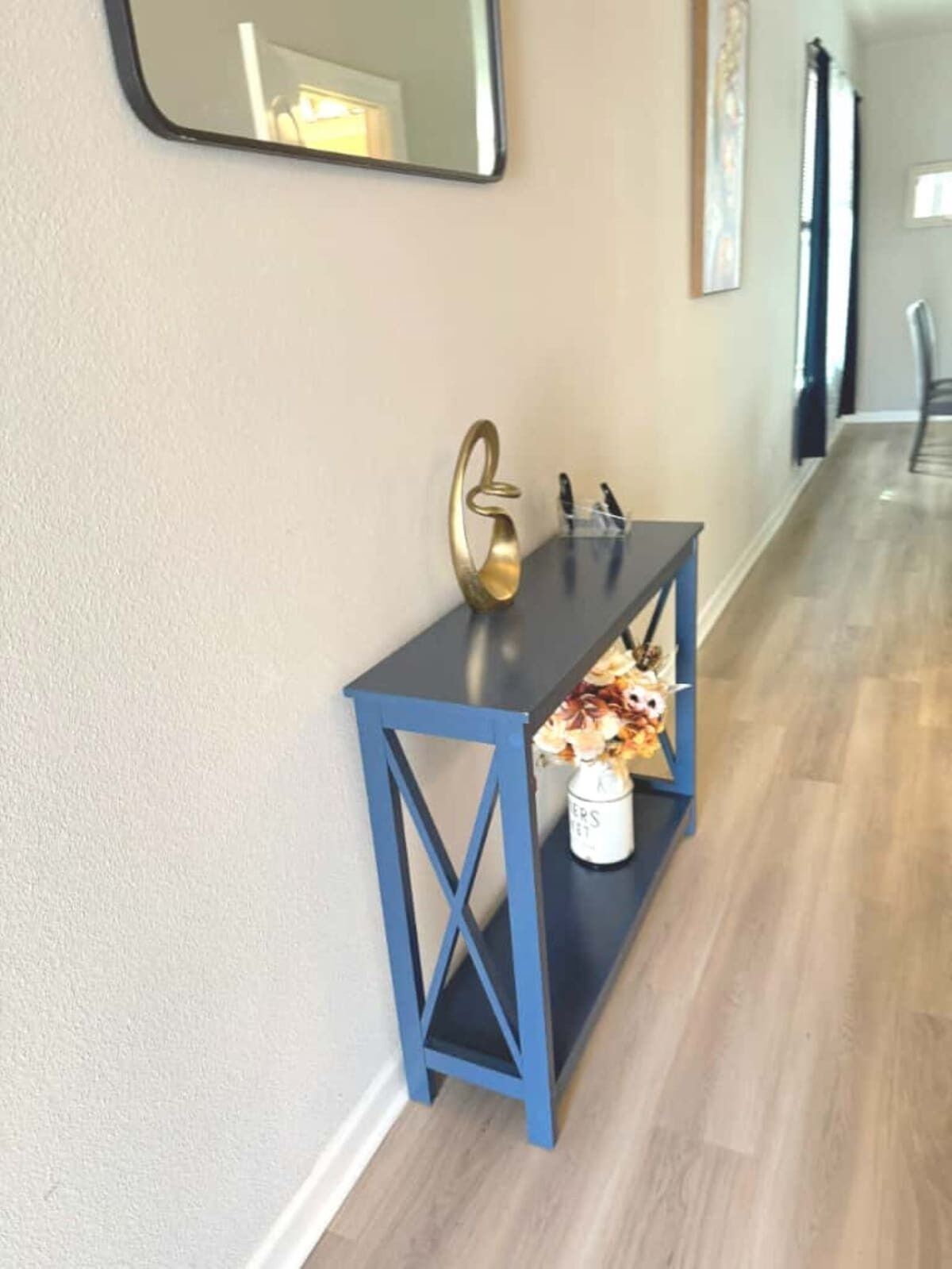 Un pasillo con una consola azul, un florero y un espejo en la pared.