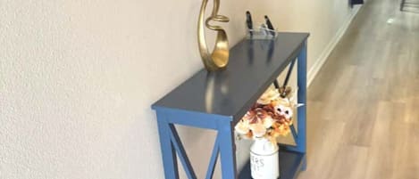 A hallway with a blue console table, a vase with flowers, and a mirror on the wall.