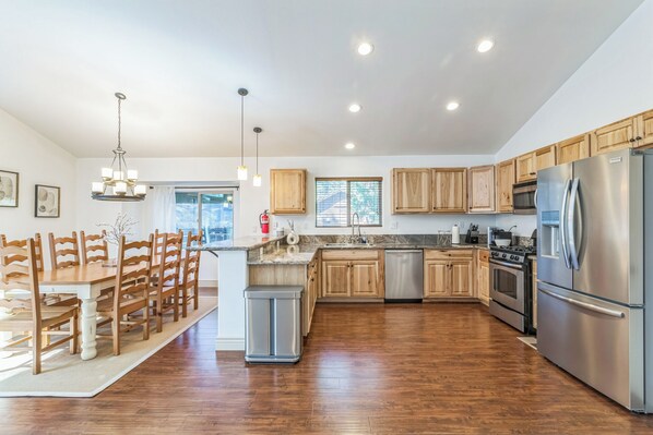 A modern kitchen with wooden cabinets, stainless steel appliances, and a dining area with wooden chairs.