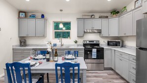 A modern kitchen with grey cabinets, a stainless steel refrigerator, a microwave, and a dining table set for four.