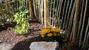 A garden with a rock, bamboo fence, and various plants including yellow and red flowers. - Lomasi, 65 sqm, 1 bedroom, ground floor, terrace (Marquartstein)