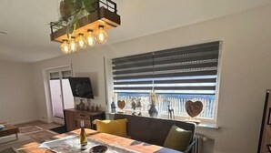 A modern kitchen with a wooden island, a dining area with a table and chairs, and a living area with a sofa and a TV. - Lomasi, 65 sqm, 1 bedroom, ground floor, terrace (Marquartstein)